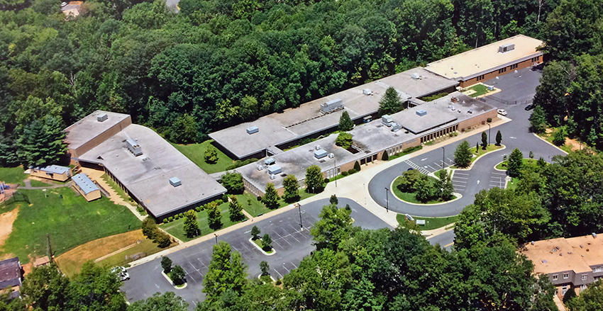 Color aerial photograph taken from a helicopter above North Shore Drive looking toward our building at an angle from due south. Compared with the earlier aerial photograph from the 1960s, you can see there have been three additions to the building: the gymnasium, and two classroom wings that have connected the formerly separate houses. 