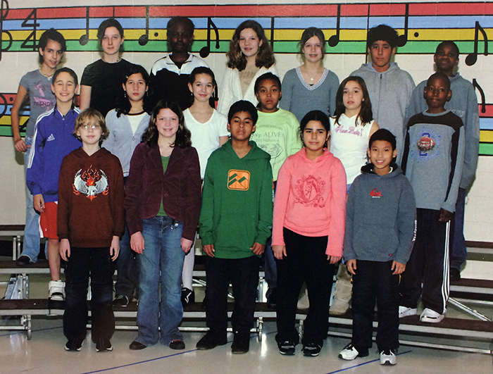 Yearbook photograph of the Lake Anne Ringers from 2005 to 2006. 18 children are pictured, standing in rows on three risers. Music notes are painted on the classroom wall behind them in colorful shades of red, blue, yellow, and green. 